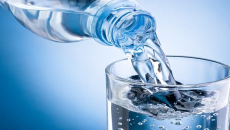 Pouring water from bottle into glass on blue background